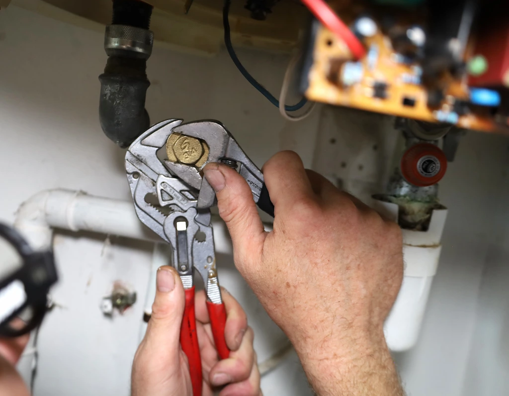 Mains d'un plombier utilisant une clé à molette pour réparer un tuyau sous un évier.
