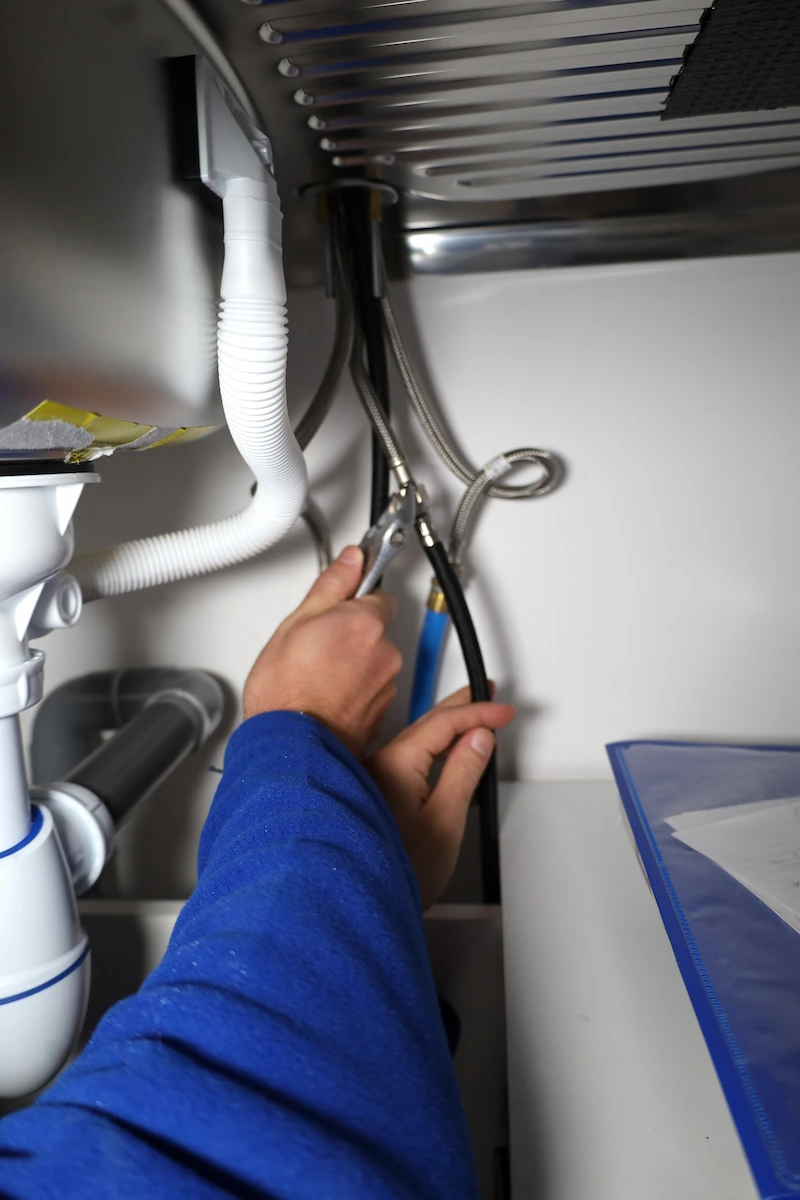 Un plombier serre un tuyau en métal sous un évier avec une pince.