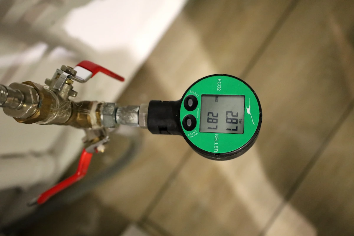 Manomètre numérique vert KELLER ECO2 affichant 2.81 BAR fixé à une vanne avec poignée rouge.