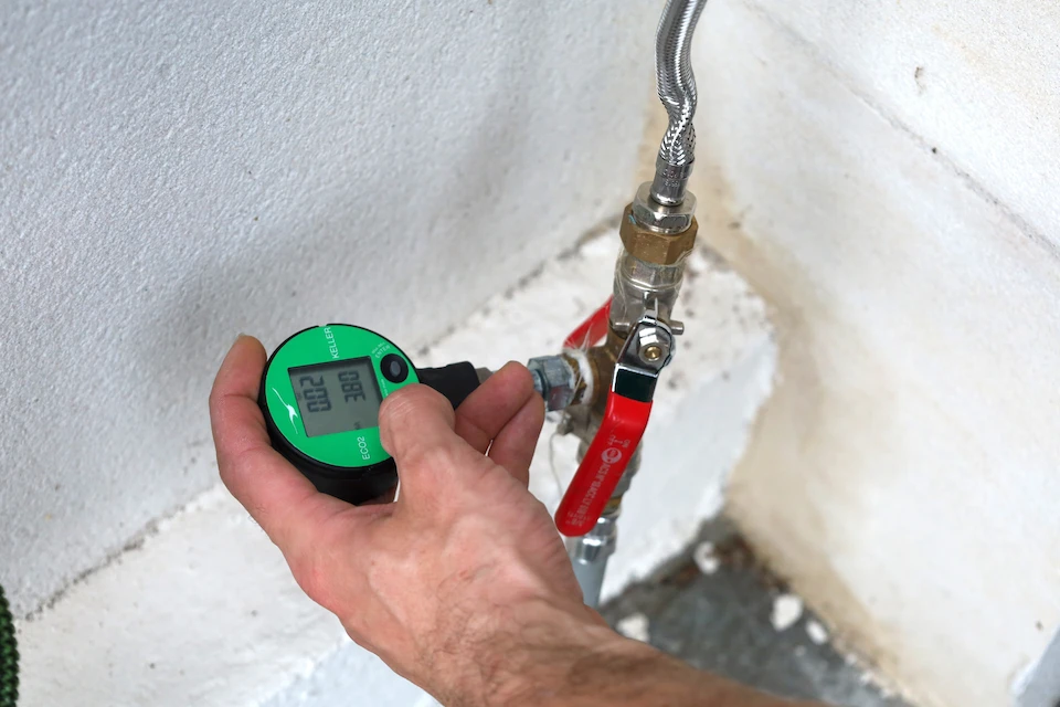 Main tenant un appareil vert de mesure de pression connecté à un robinet avec une poignée rouge.