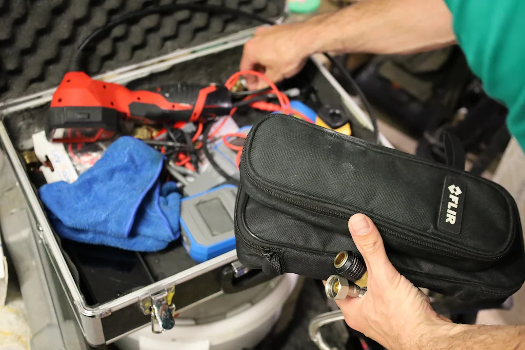 Une personne tient une trousse noire FLIR au-dessus d'une mallette contenant divers outils et un chiffon bleu.