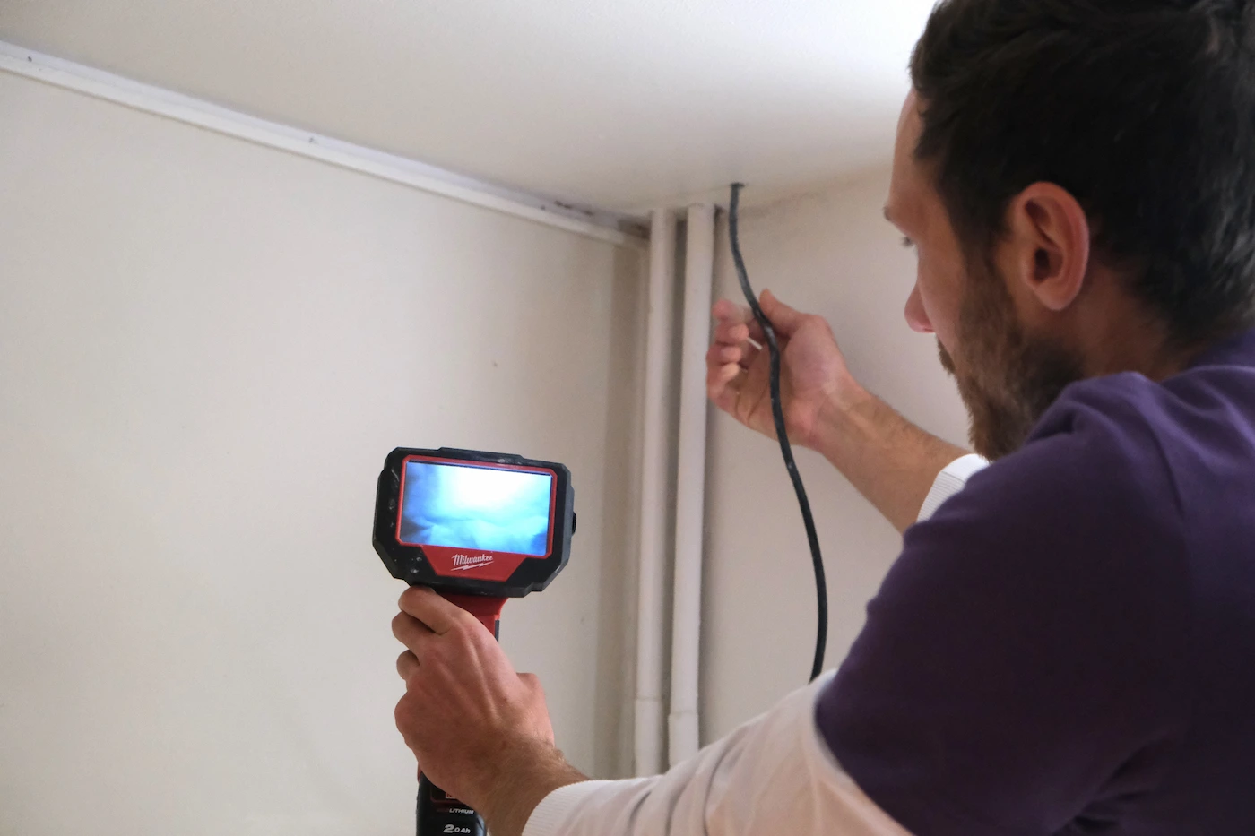 Un homme utilise une caméra d'inspection pour examiner un tuyau dans un coin de mur intérieur.