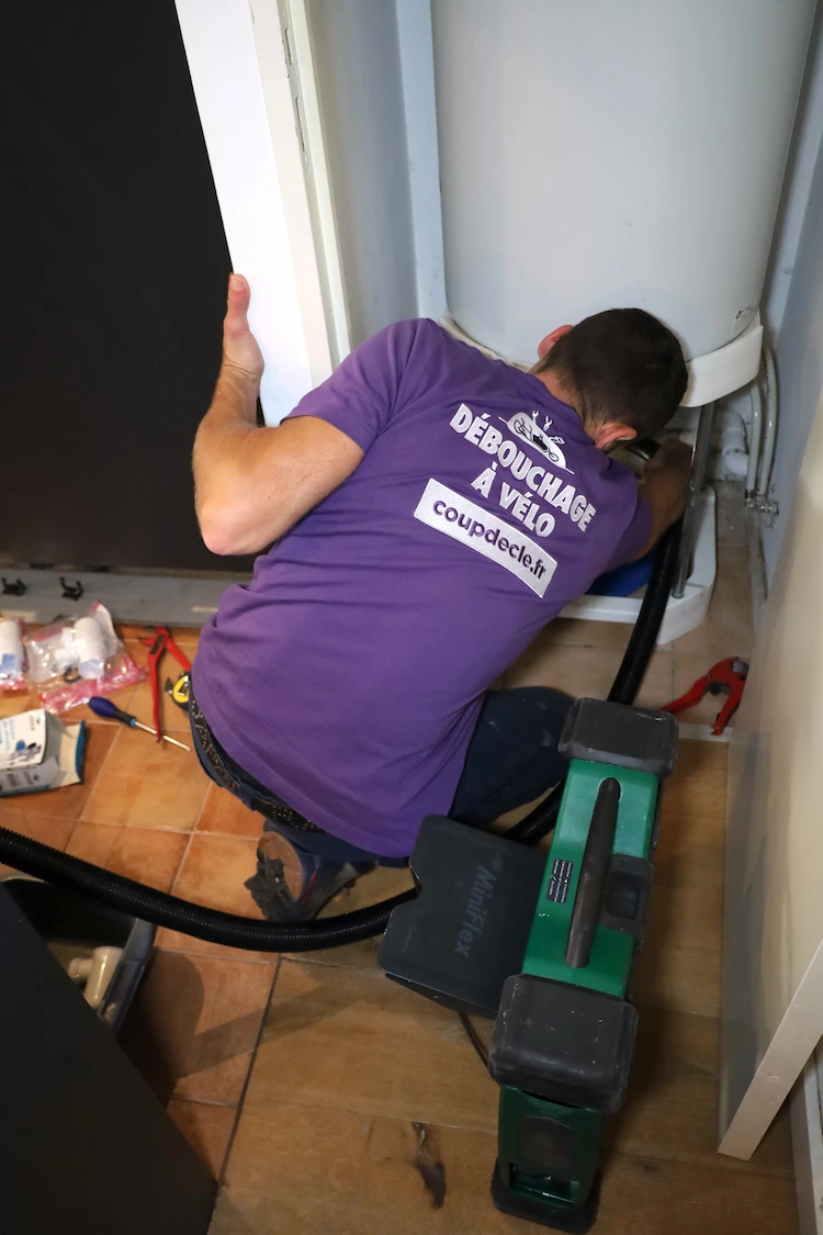 Technicien en t-shirt violet effectuant un débouchage de chauffe-eau avec une machine spécialisée.