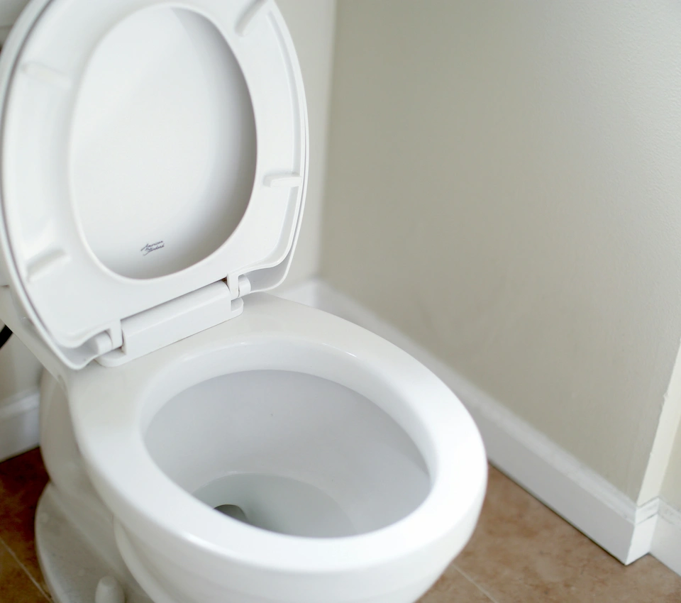 Toilette blanche avec abattant ouvert dans une salle de bain aux murs clairs.
