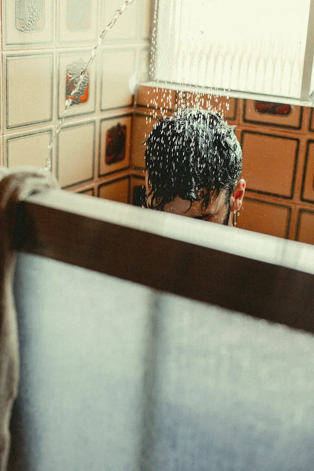 Homme prenant une douche dans une salle de bain avec des carreaux aux motifs vintage.