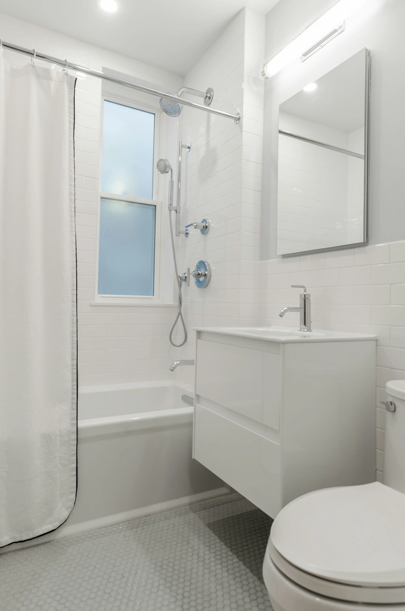 Salle de bain blanche avec baignoire, rideau de douche, lavabo avec miroir et toilettes modernes.