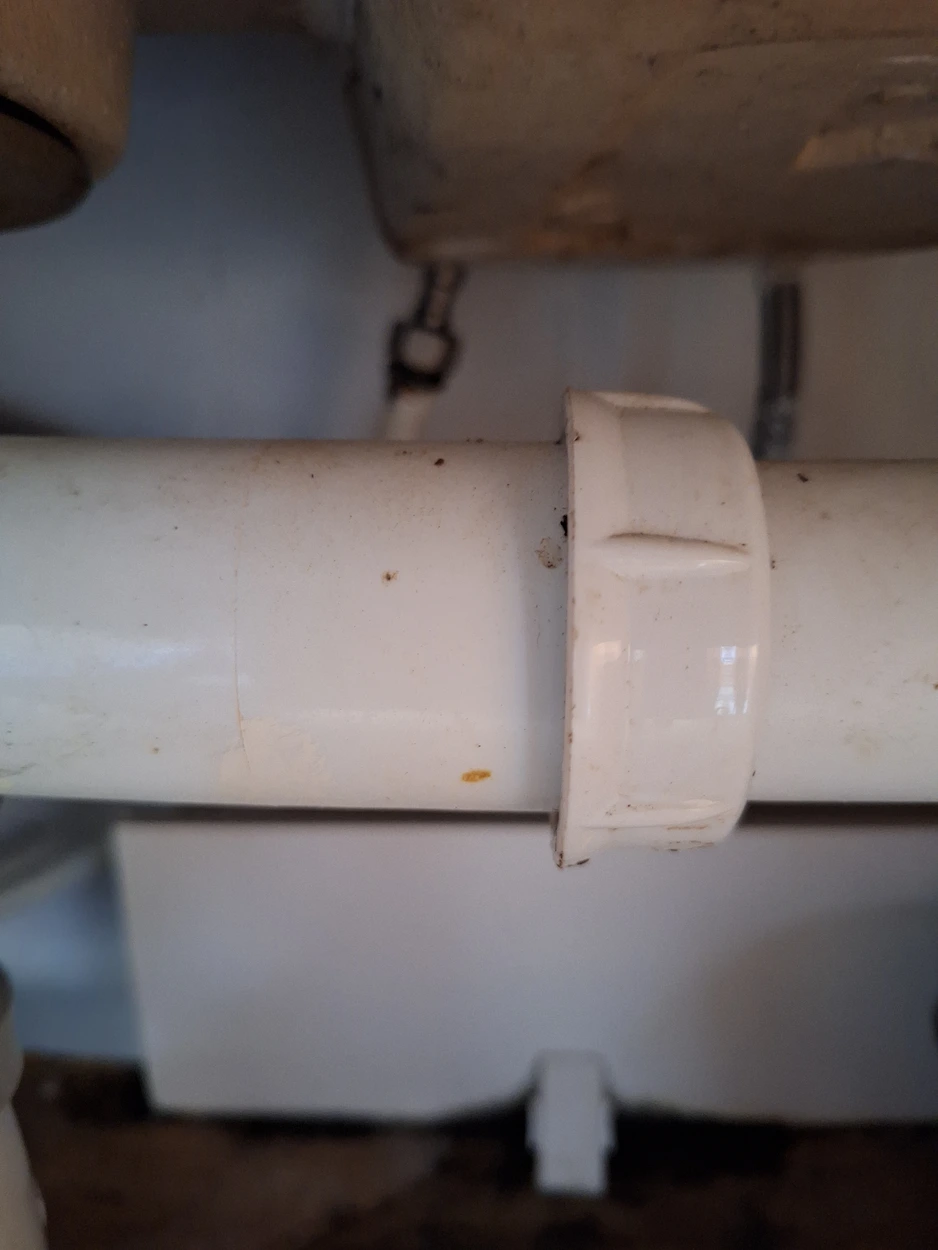 Gros plan sur un tuyau en plastique blanc avec un collier de serrage, sous un lavabo.