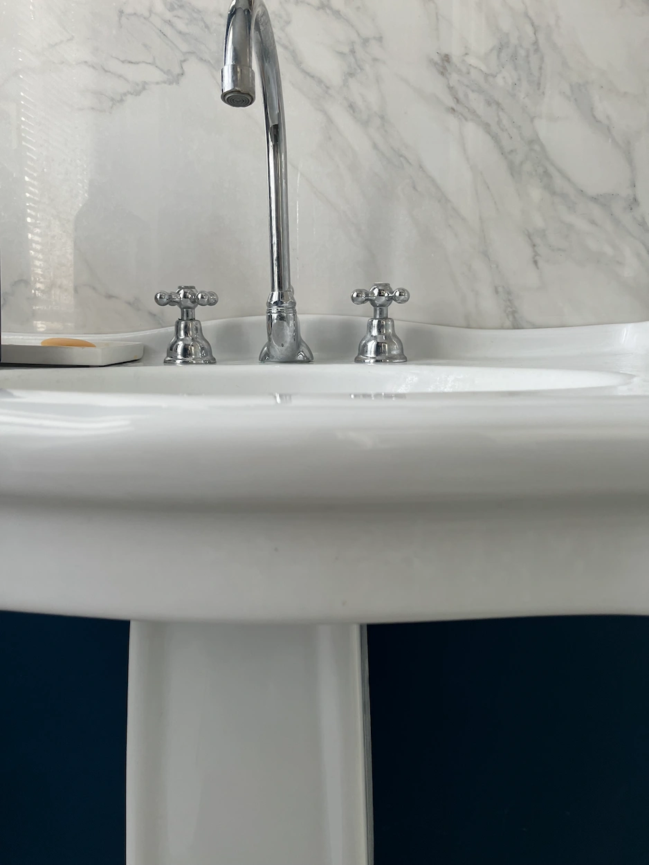 Lavabo blanc avec robinetterie vintage chromée et mur effet marbre en arrière-plan.