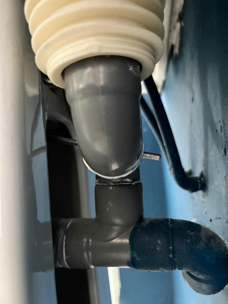 Tuyaux en PVC gris sous un lavabo contre un mur bleu.