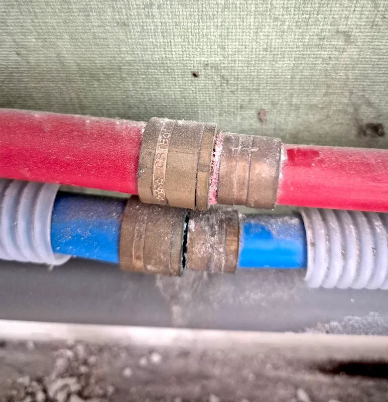 Raccords de canalisation avec tuyau rouge et bleu montrant des dépôts blancs autour des jonctions.