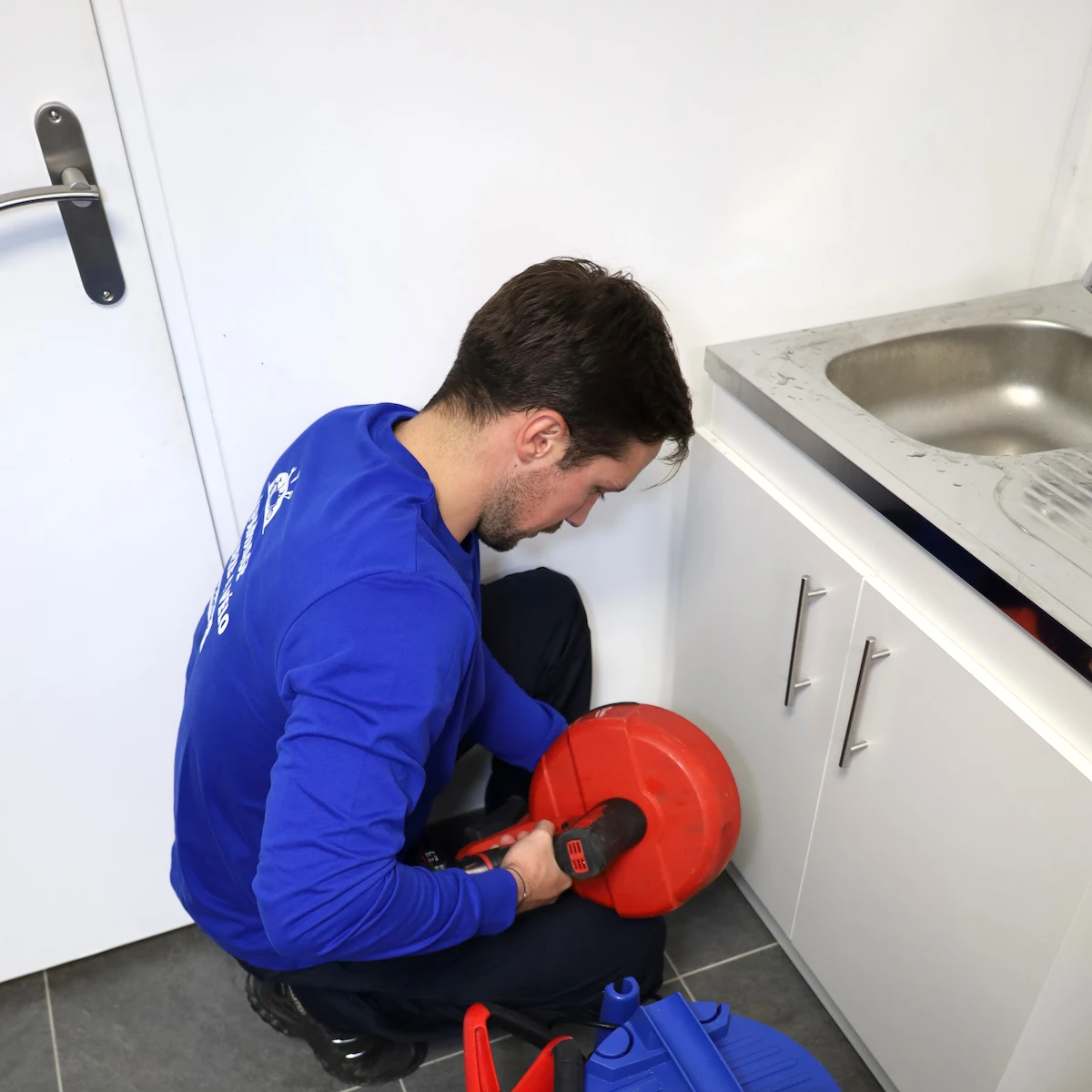 Plombier portant une t-shirt bleu réparant le mécanisme d'un WC suspendu