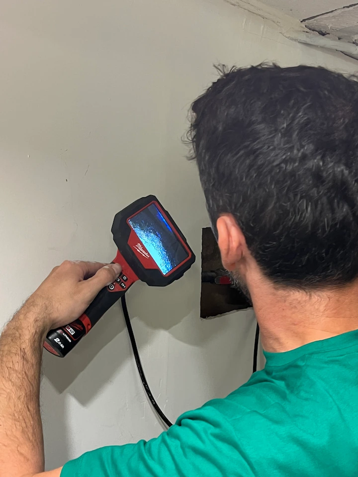 Homme utilisant une caméra d'inspection Milwaukee pour examiner l'intérieur d'un mur à travers une ouverture rectangulaire.