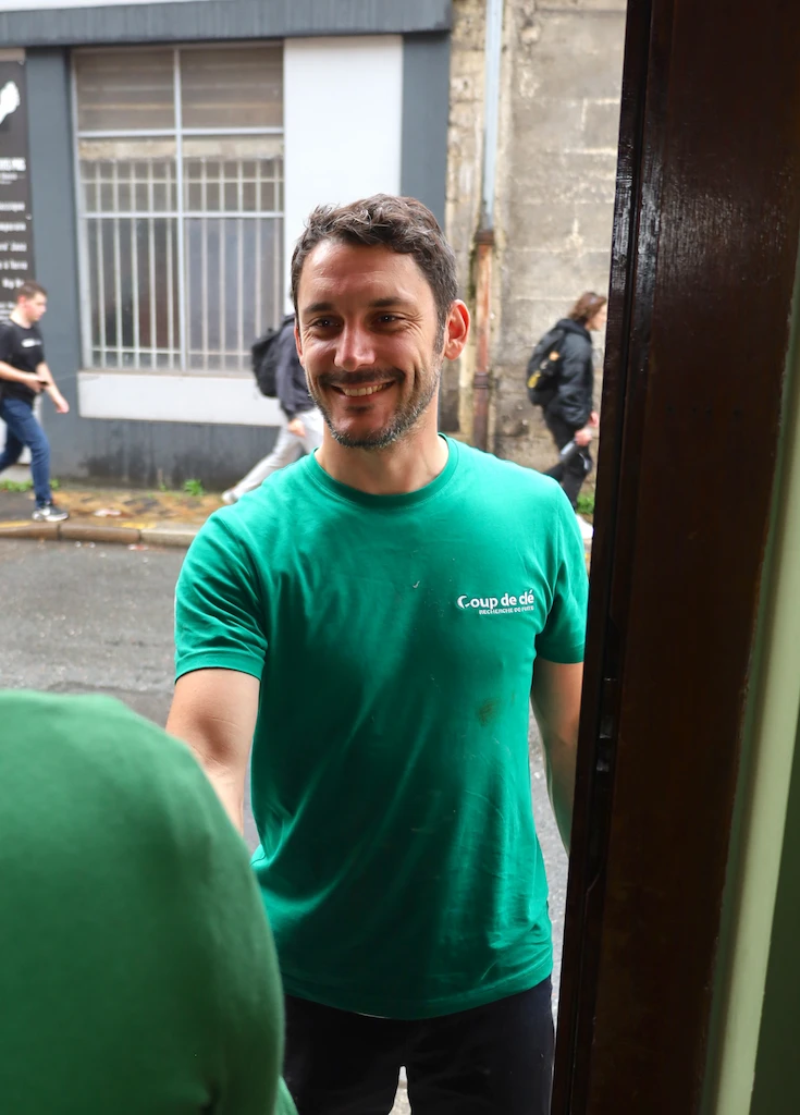 Un technicien souriant en t-shirt vert saluant un client devant une porte ouverte.