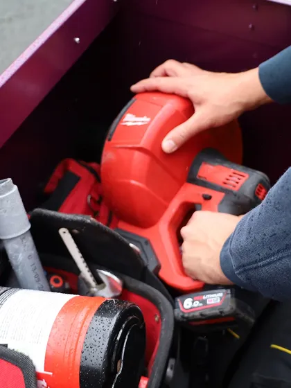 Main tenant un outil électrique rouge Milwaukee dans une caisse à outils.