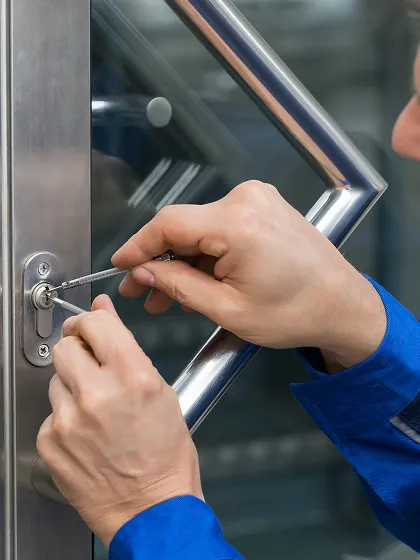 Person en combinaison bleue crochetant une serrure métallique d'une porte vitrée.