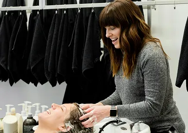 Une coiffeuse lave les cheveux d'une cliente allongée dans un fauteuil au salon.
