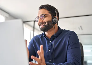Homme souriant portant un casque avec micro, en train de parler devant un ordinateur portable.