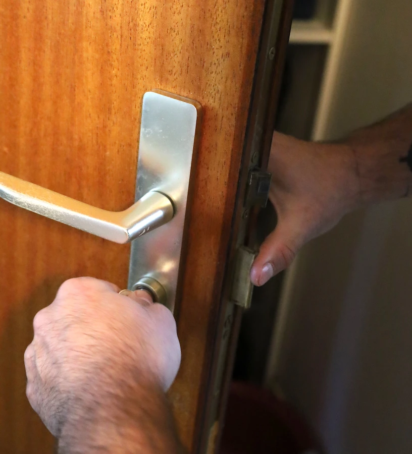 Une main tourne une clé dans la serrure d'une porte en bois avec une poignée métallique.