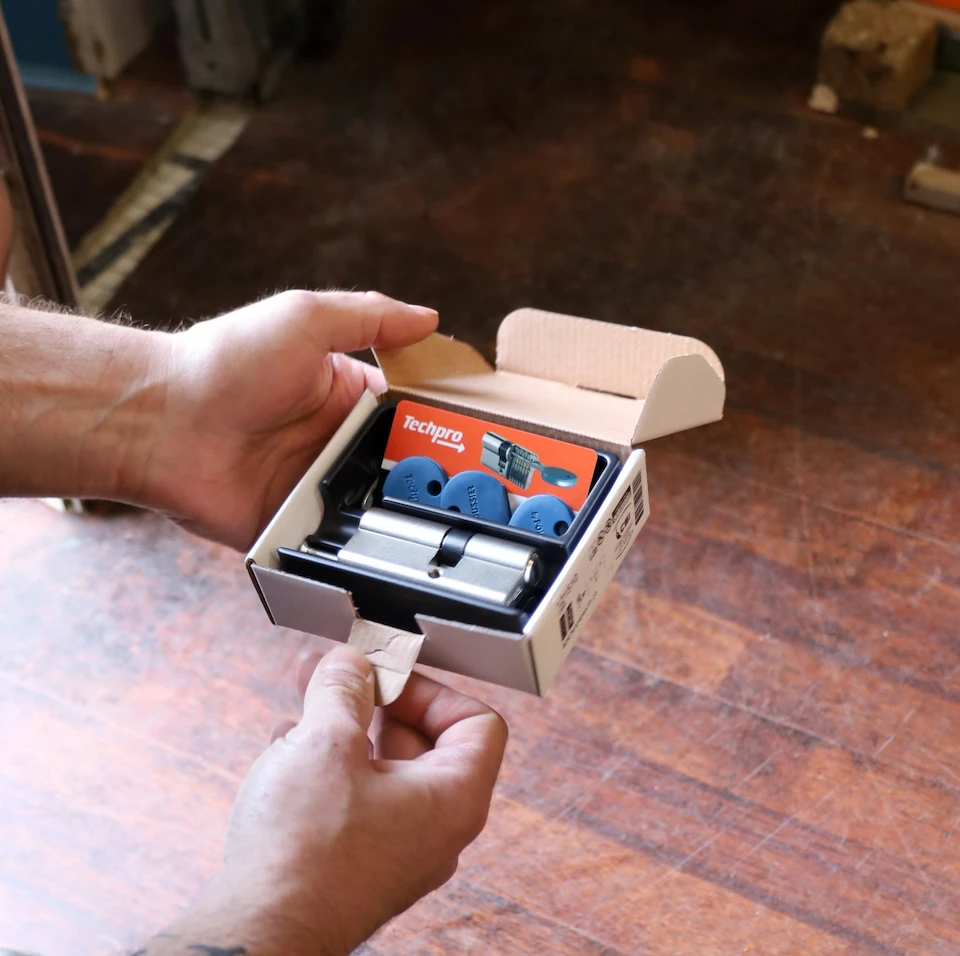 Mains tenant une boîte ouverte contenant un cylindre de serrure et des embouts bleus Techpro.