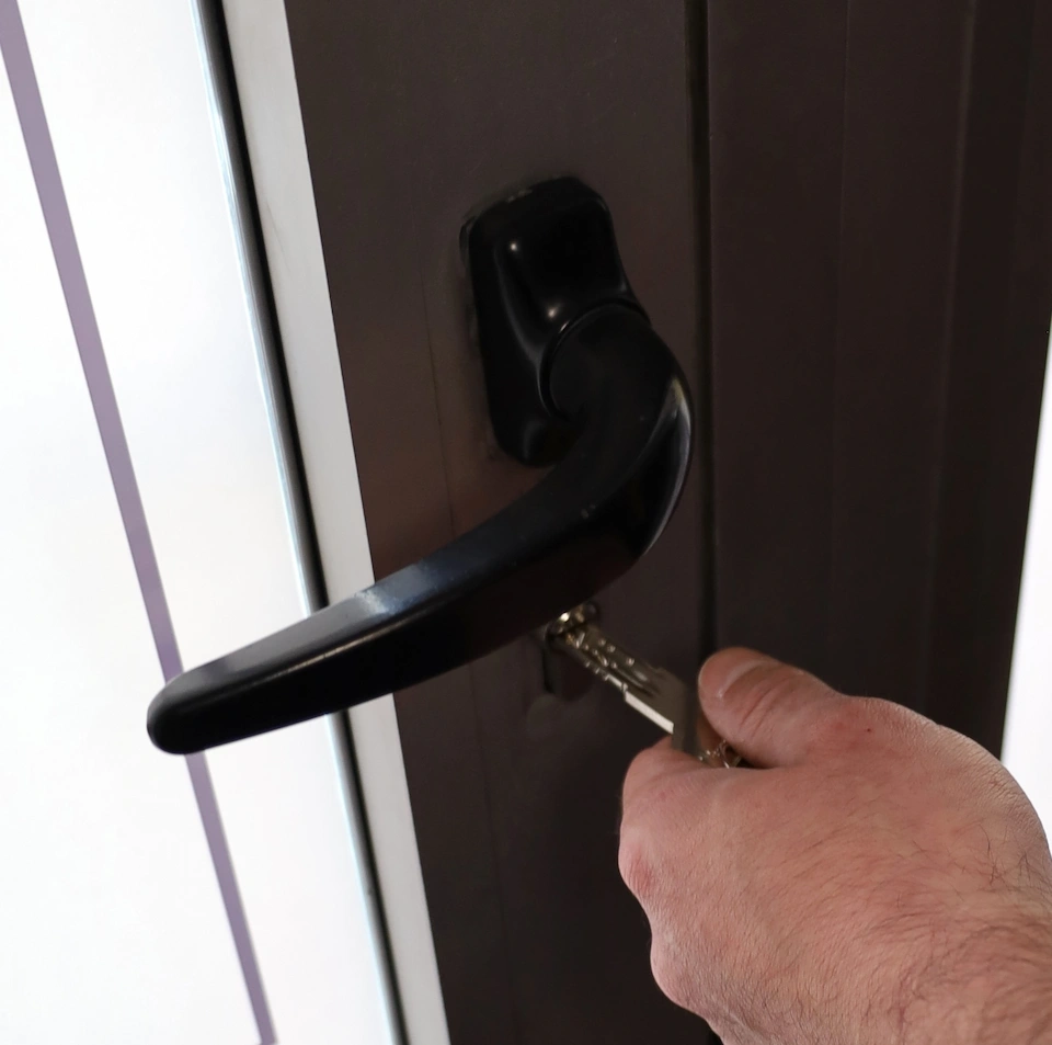 Main insérant une clé dans la serrure d'une porte noire avec une poignée noire.