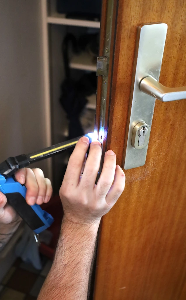 Technicien serrurier Coup de clé utilisant un outil lumineux pour réparer une serrure de porte en bois à Bordeaux.