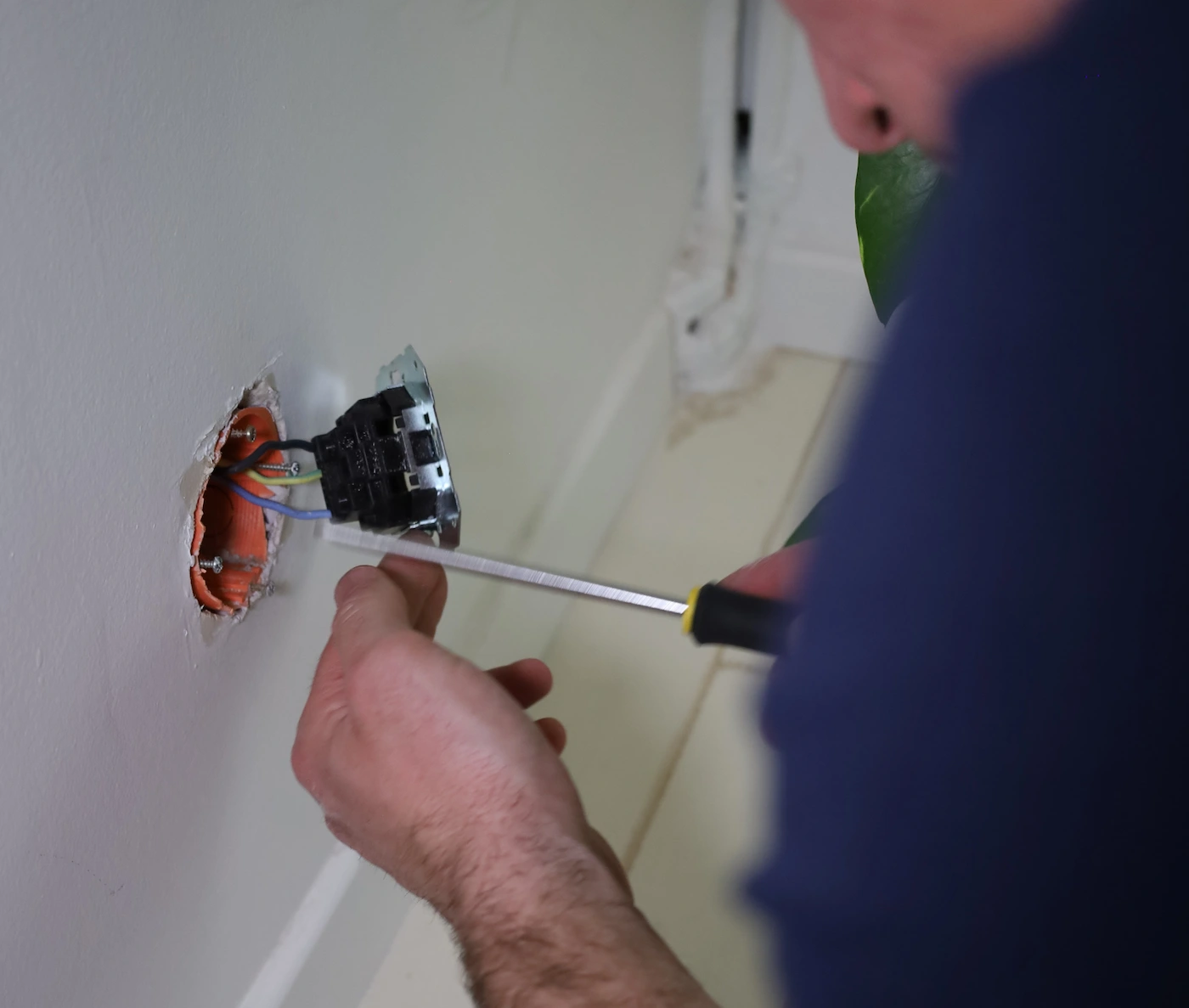 Une personne répare une prise électrique murale avec un tournevis.