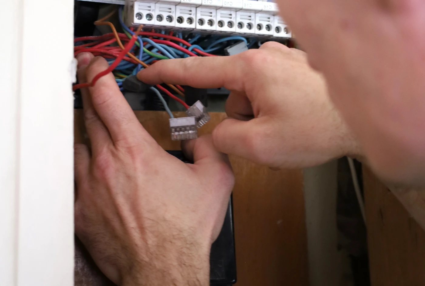 Mains travaillant sur des fils à l’intérieur d’un tableau électrique avec des disjoncteurs et des connecteurs.