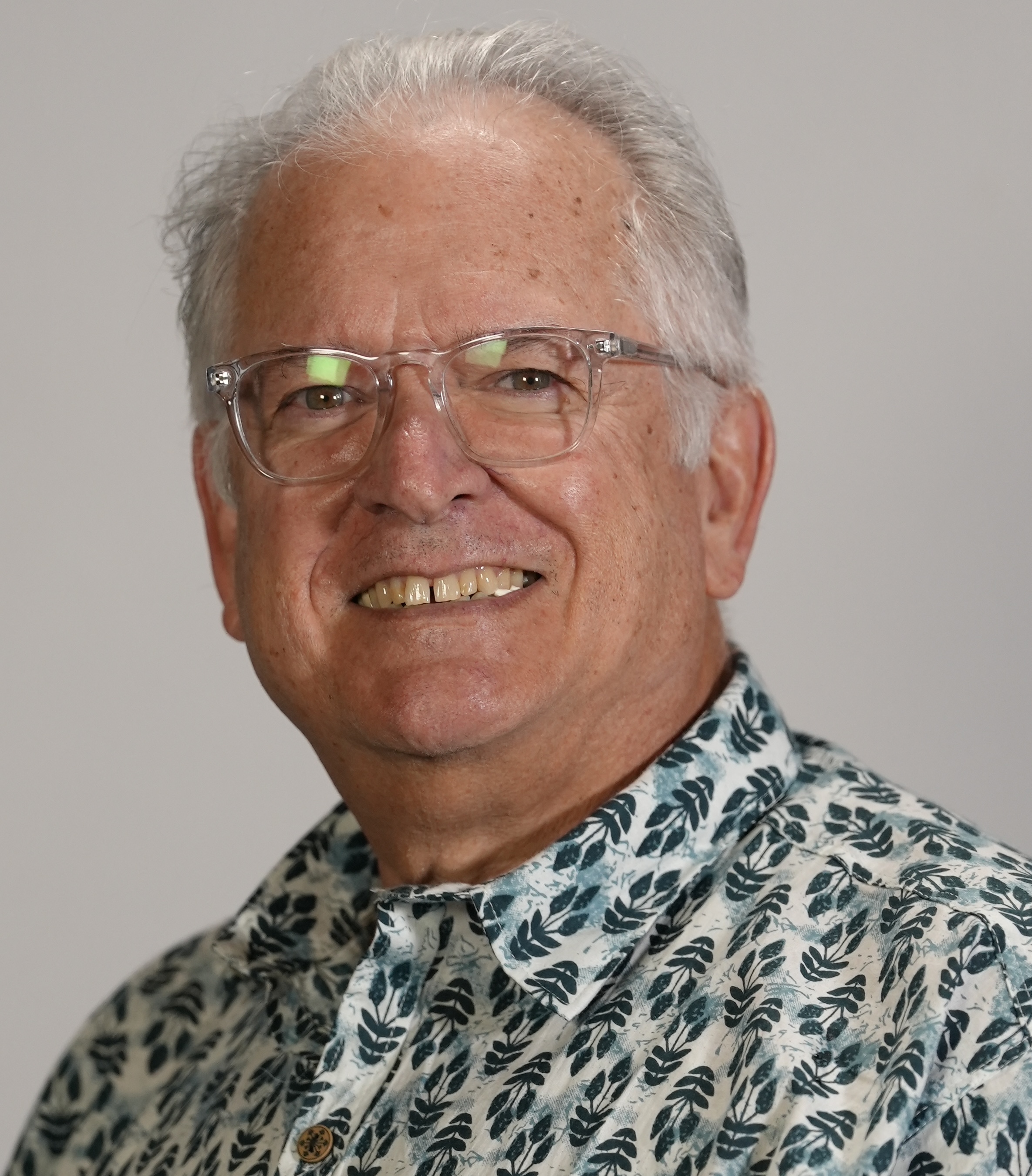 Ramon smiles big while wearing his clear glasses, and flower print shirt with teal and light blue