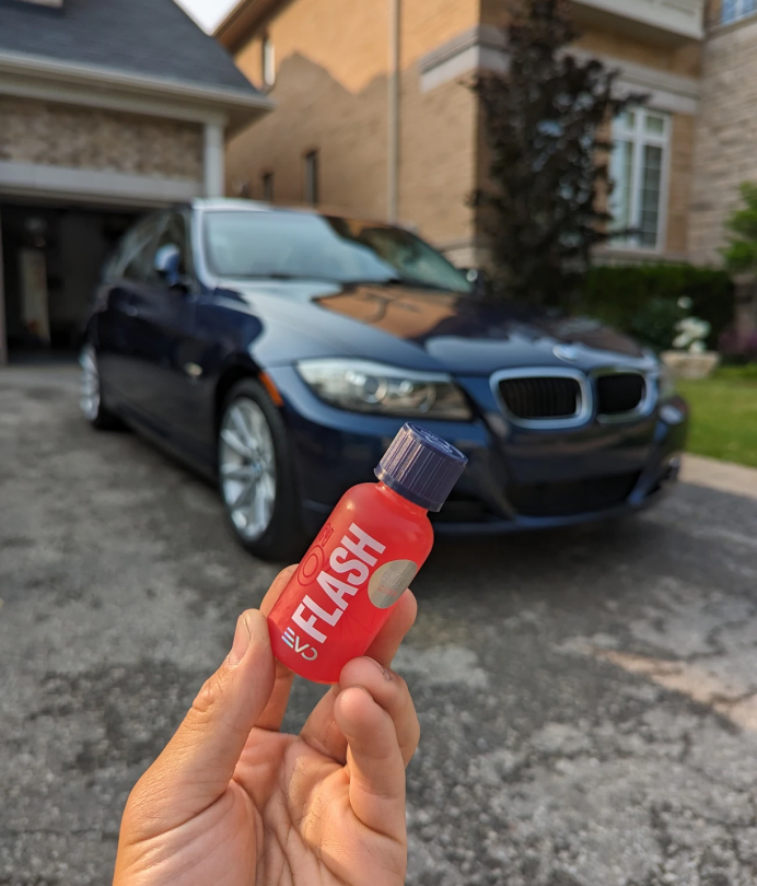 A hand holding a small lip bale in front of a car.