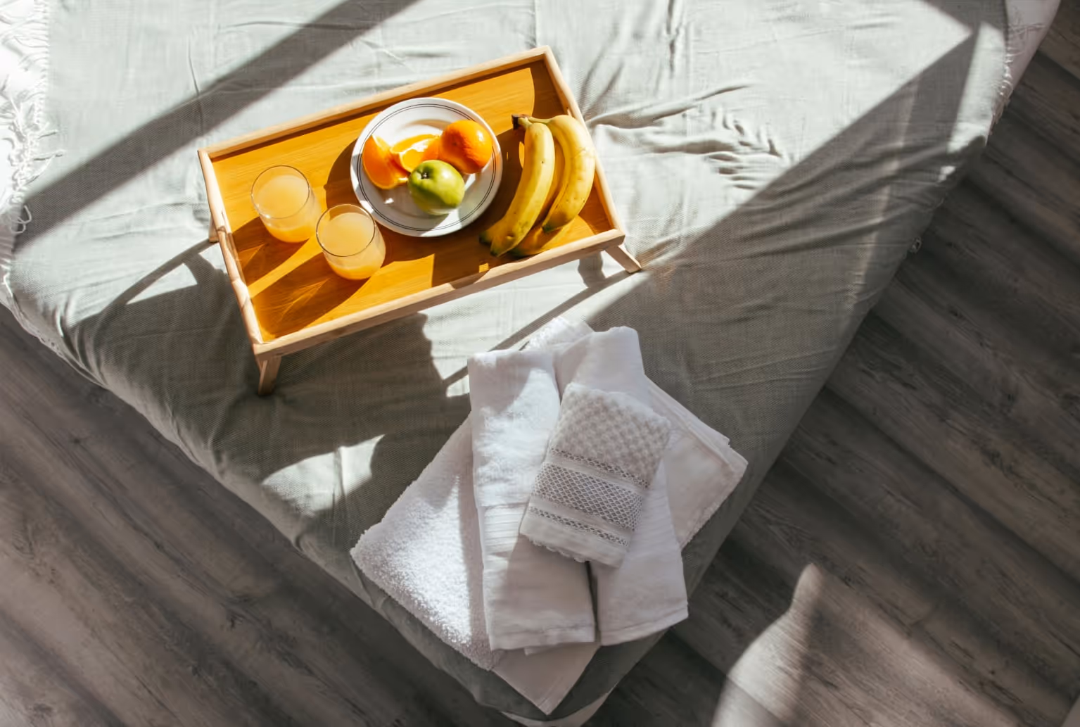 A tray of fruit and a bowl of fruit on a bed.