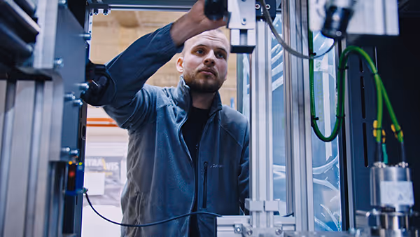 Ein Mann in Arbeitskleidung bedient eine industrielle Maschine in einer Produktionsumgebung – symbolisiert technische Facharbeit oder Anlagenbedienung im industriellen Bereich.