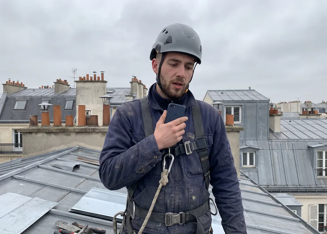 Couvreur-zingueur sur un toit en zinc à Paris, harnaché, qui parle dans son téléphone