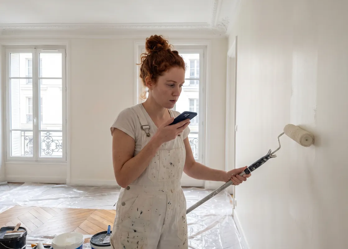 Peintre en bâtiment dans un appartement parisien rénové, qui dicte une note sur son téléphone
