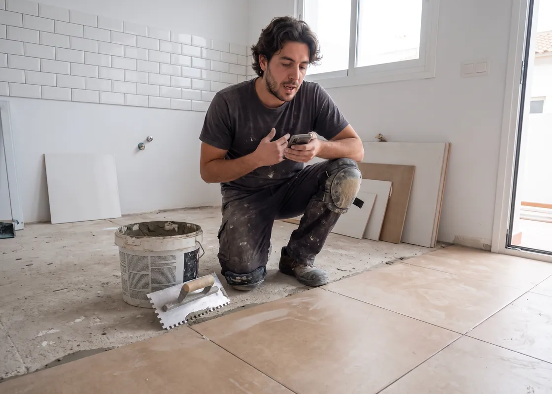 Alicatador colocando baldosas de porcelánico en una cocina, dictando una nota en su móvil