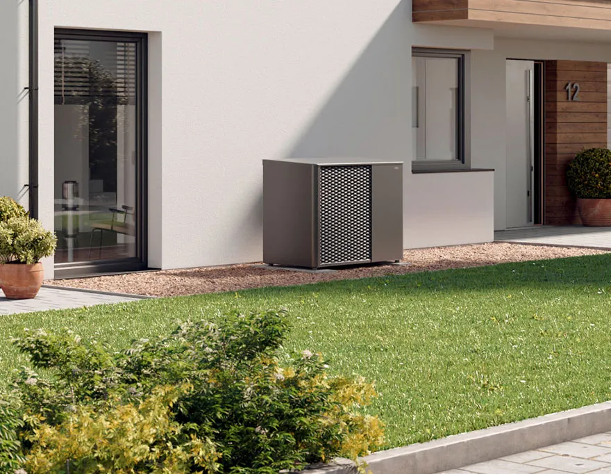 Moderne Wärmepumpe der Marke LG vor einem weißen Haus mit Glasfenstern und grünem Rasen.