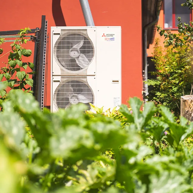 Blick auf ein modernes Stadthaus mit Solarpaneelen auf dem Flachdach, umgeben von einem gepflegten Garten mit Bäumen und Sträuchern.