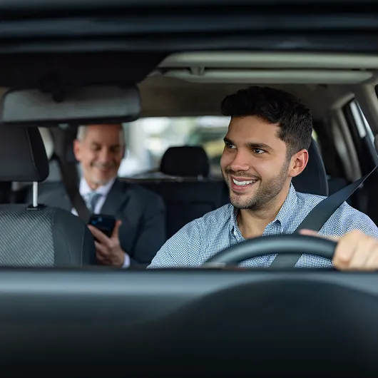 Chauffeur souriant conduisant un client assis à l’arrière d’une voiture