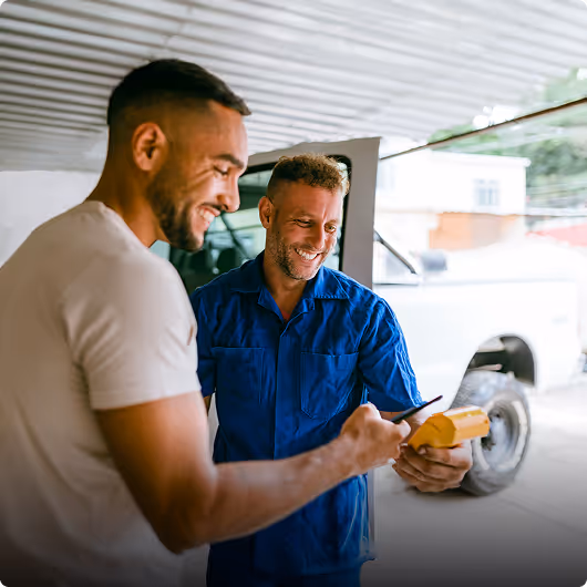 Deux mécaniciens souriants utilisant un appareil de diagnostic dans un garage automobile