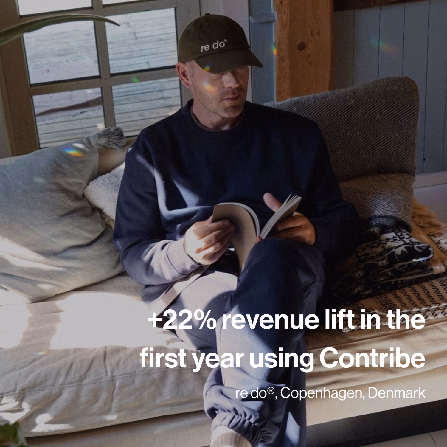 Man wearing a black cap and navy outfit sitting on a couch reading a book.