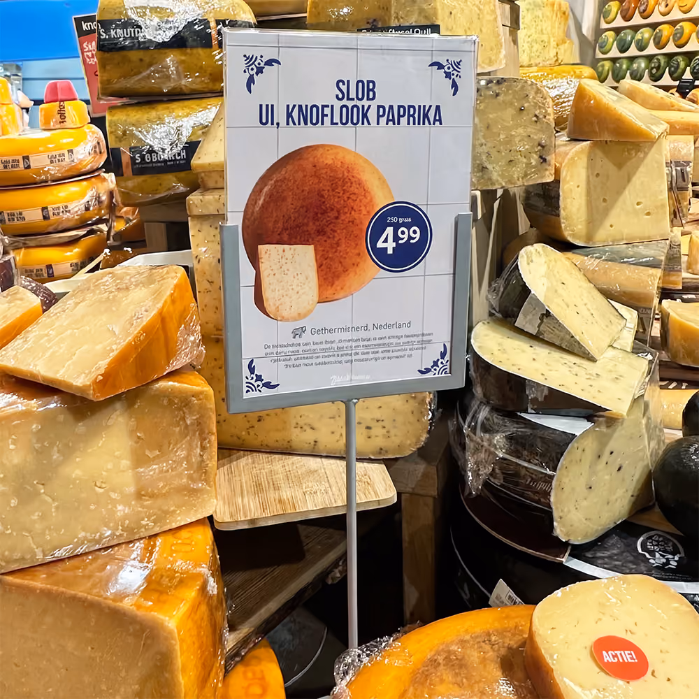 In-store reclamebord voor kruidenkaas tussen uitgestalde kaaswielen