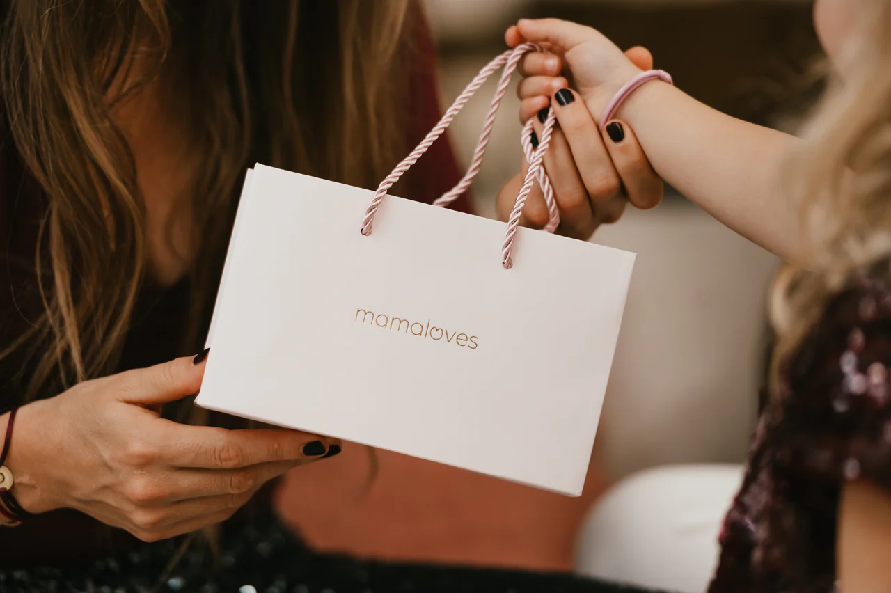 Twee vrouwen wisselen een cadeautasje van het merk mamaloves uit