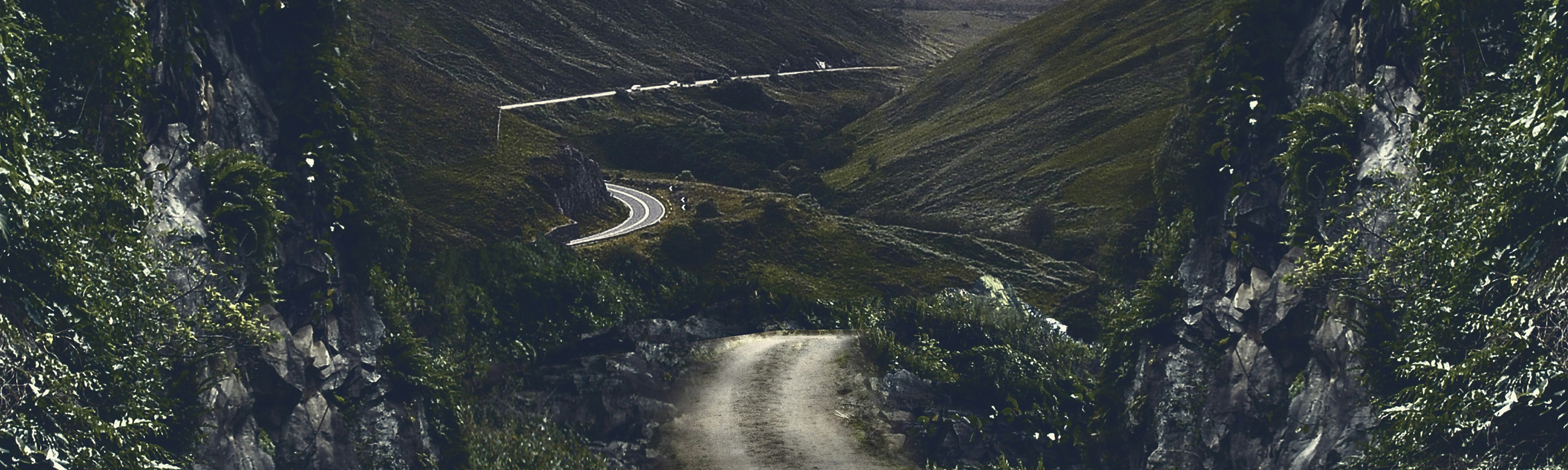 Photo of a winding dirt road in a countryside with rolling hills.