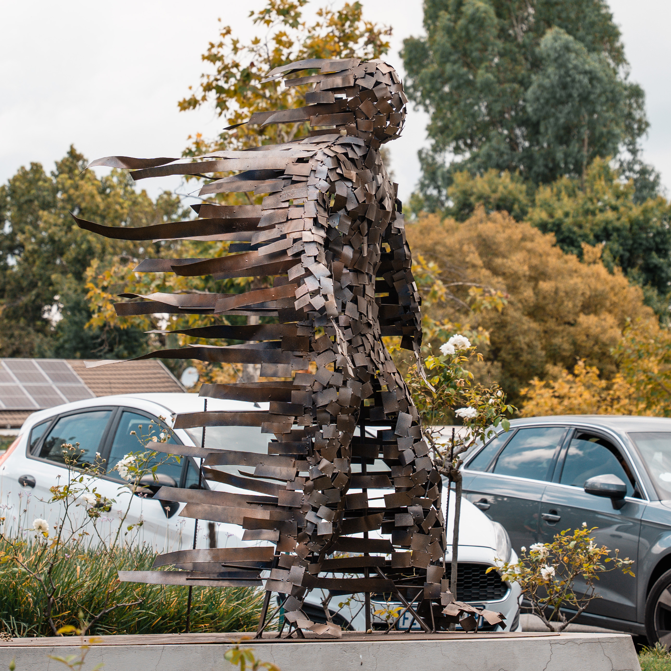 A steel sculpture formed by layering hundreds of small steel plates and ribbons to create an abstract figure walking into the wind.