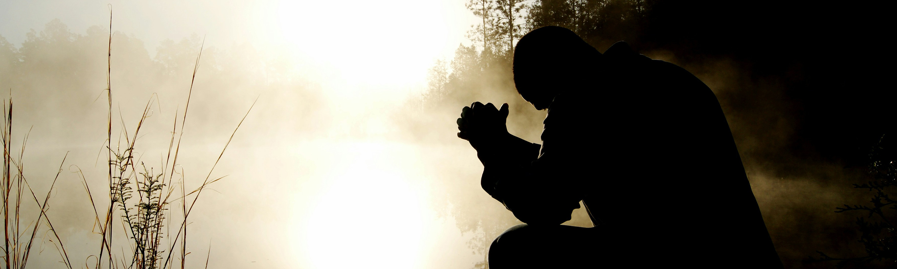 Man praying during a misty sunrise.