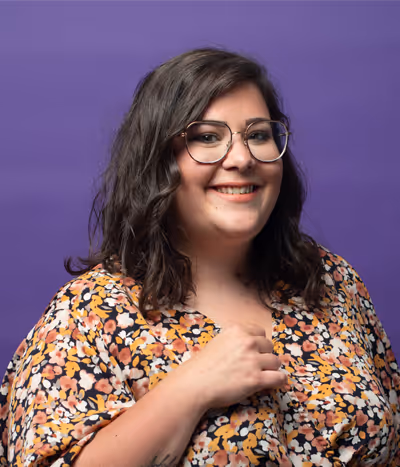 Romane Le Treut, designer graphique à l'agence, de face sur un fond mauve, souriante