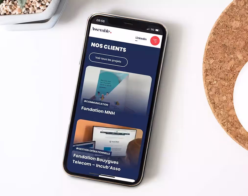 Un téléphone portable placé sur une table blanche ouvert sur la page d'accueil du site Assemble