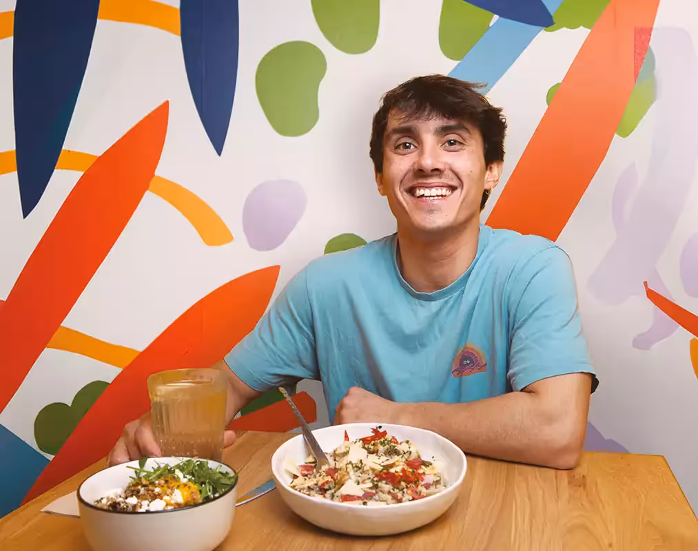 Photo d'un consomateur de l'enseigne Izee dans les locaux, avec le sourire, assis devant une table ronde, entrain de déguster un plat