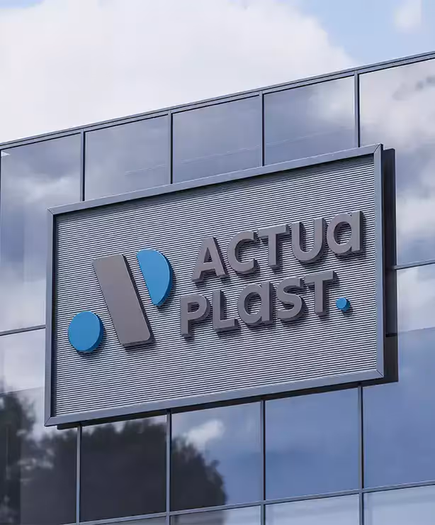 Logo Actuaplast monté sur un mur en verre reflétant le ciel, sur un bâtiment professionnel.
