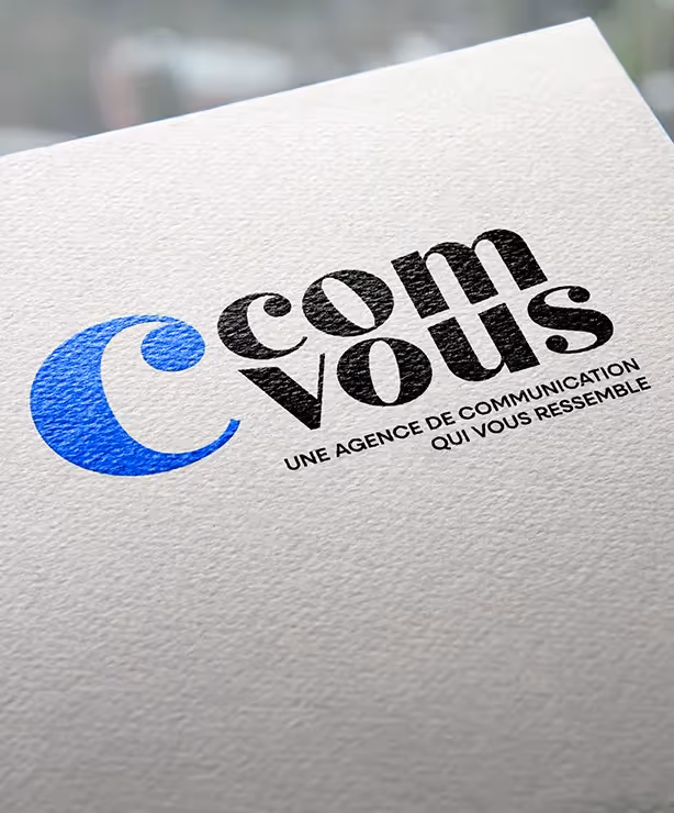 Zoom sur le logo C’ComVous imprimé en noir et bleu sur papier texturé, avec le slogan « Une agence de communication qui vous ressemble ».