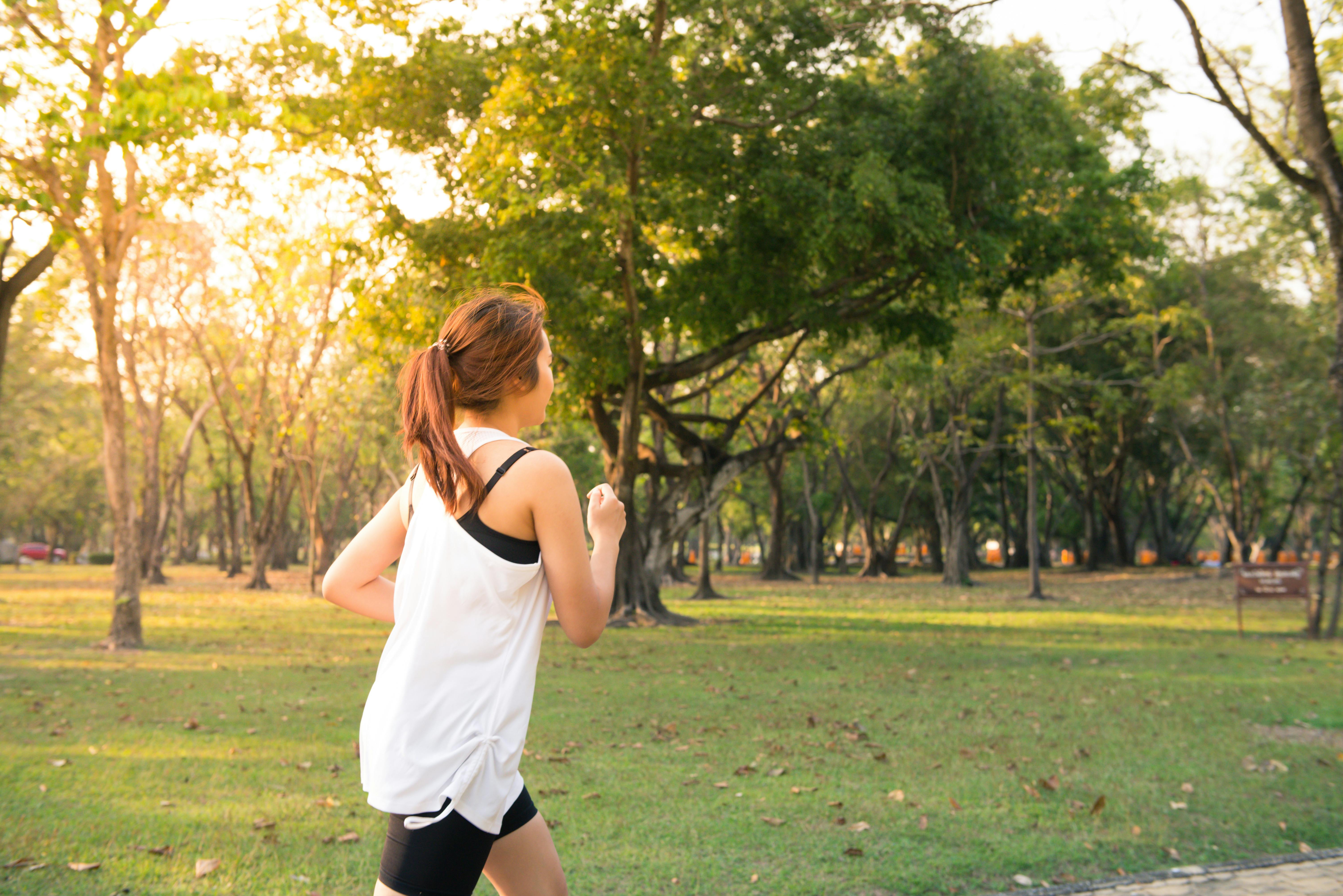 Frau joggt bei Sonnenuntergang durch einen grünen Park, umgeben von Bäumen und Natur.